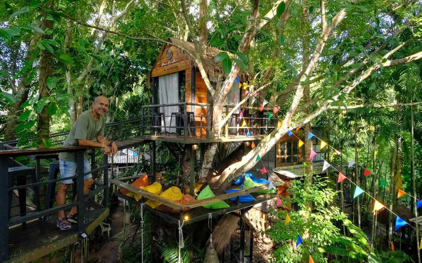 Owner standing on the treehouse walkway at Baan Ton Mai jungle cafe surrounded by lush greenery